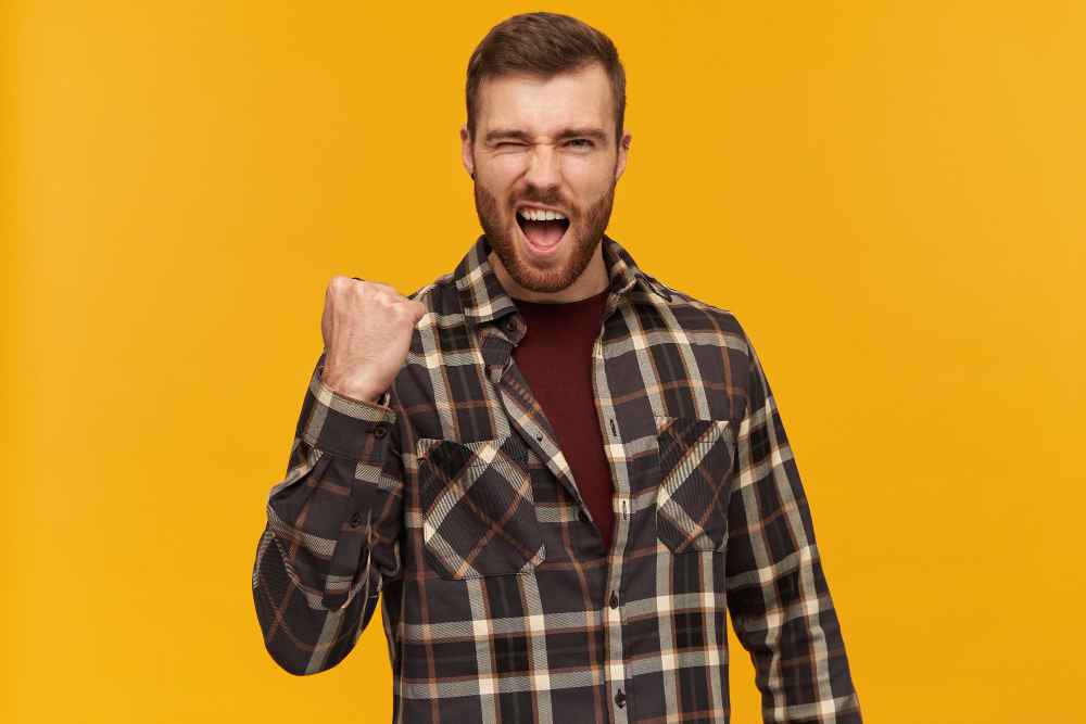 portrait handsome successful male with brunette hair bristle wearing checkered shirt accessories raises fist celebration isolated yellow wall 11zon