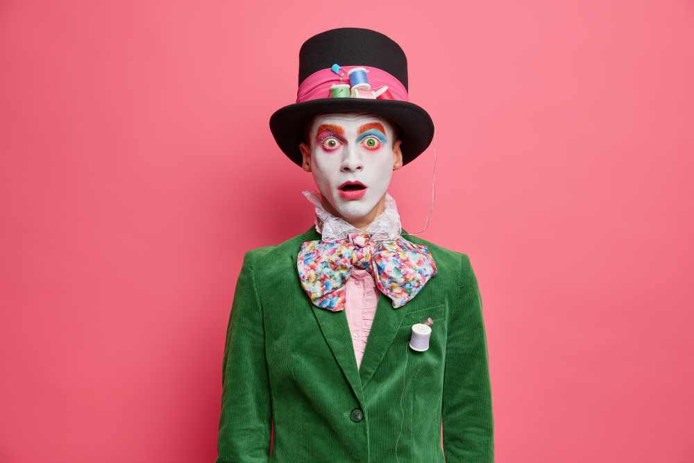 shocked embarrassed hatter stares camera with bugged eyes dressed green jacket bowtie big hat has colorful makeup takes part performance isolated rosy wall 11zon