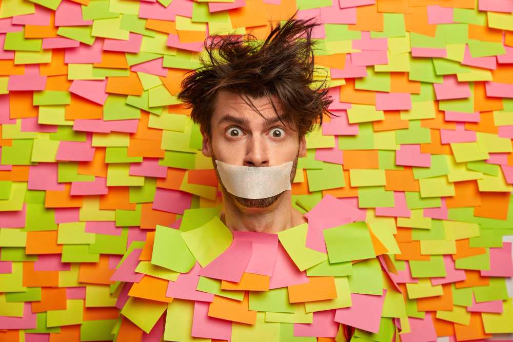 surprised nervous man with adhesive duct tape mouth asks be silent stands silenced speechless poses against colorful wall with sticky notes being frightened shut up censorship 11zon